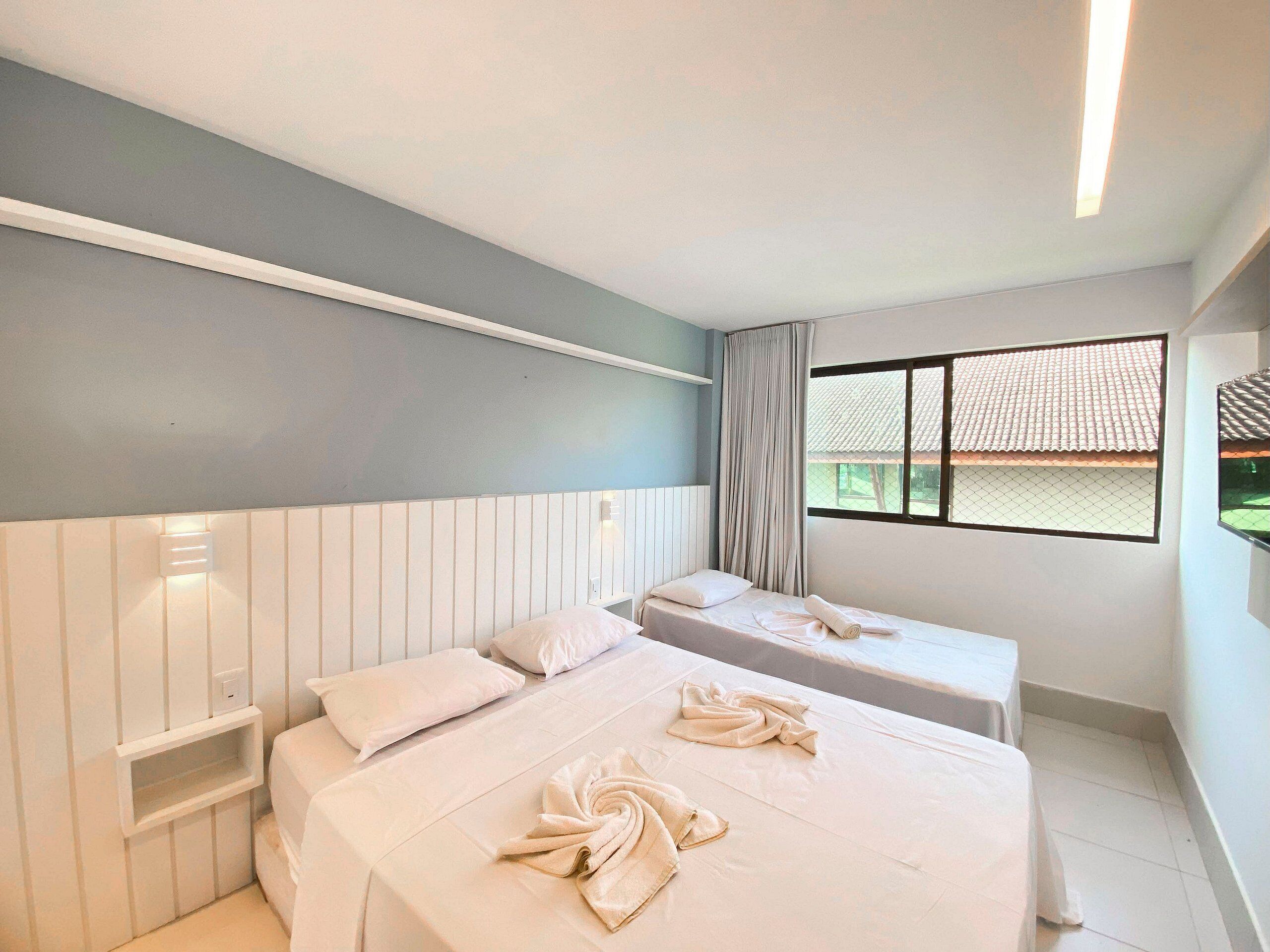 Une chambre d’hôtel avec deux lits, une fenêtre donnant sur un toit recouvert de tuiles et un mur blanc avec un interrupteur.