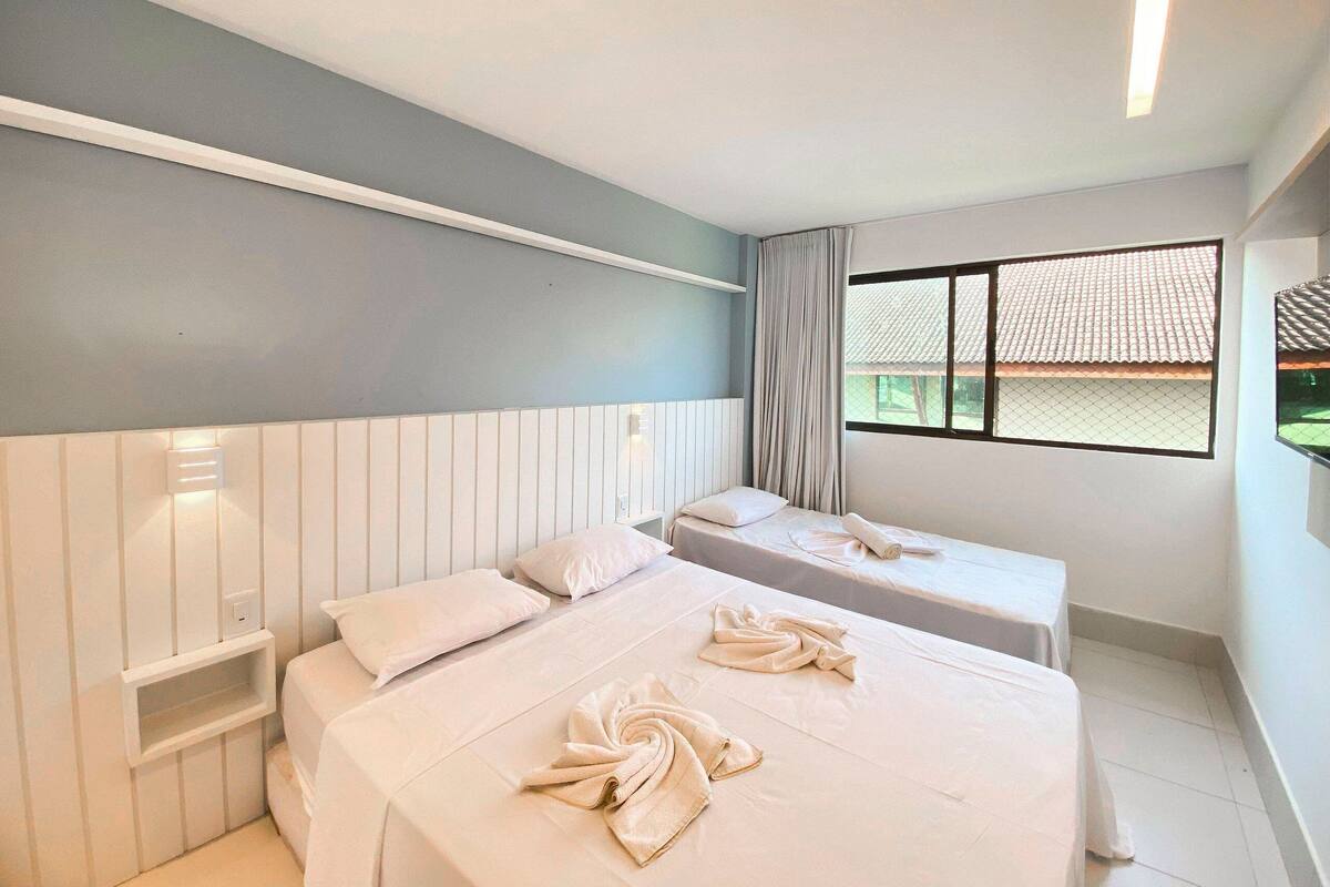 Habitación de hotel con dos camas, una ventana que da a un tejado de tejas y una pared blanca con interruptor de luz.