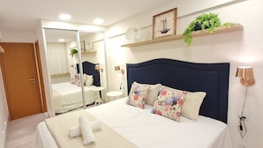 Un dormitorio con cama, mesita de noche, espejo y una ventana pequeña.