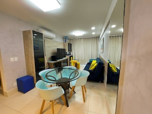 A compact living space with a dining table, chairs, a sofa, a TV, and a small kitchen area.