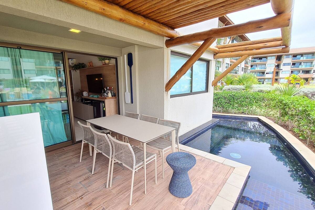 Un espacio exterior techado con piscina, una mesa de comedor con sillas y una zona de cocina.