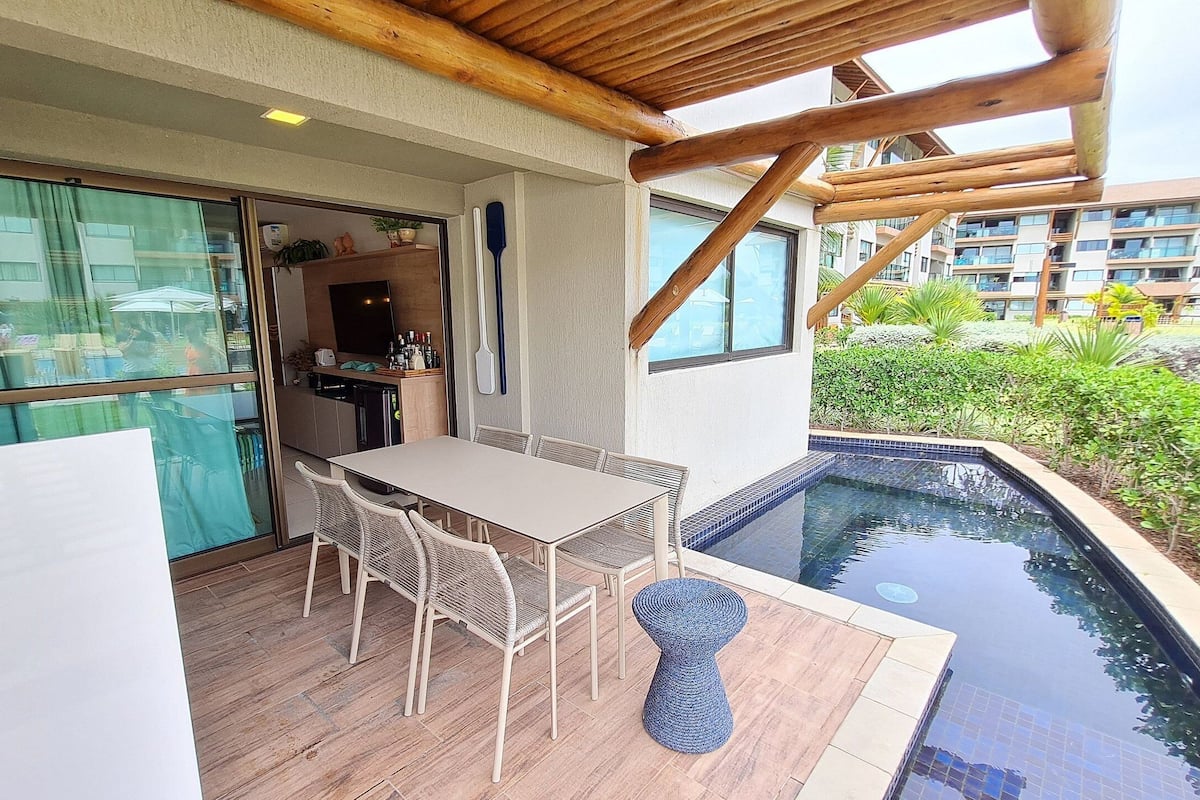 Un espacio exterior techado con piscina, una mesa de comedor con sillas y una zona de cocina.