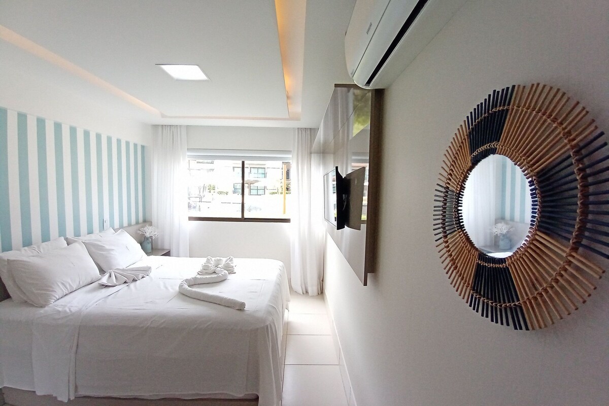 A hotel room with a bed, a wall-mounted TV, a large mirror, and a window with curtains.