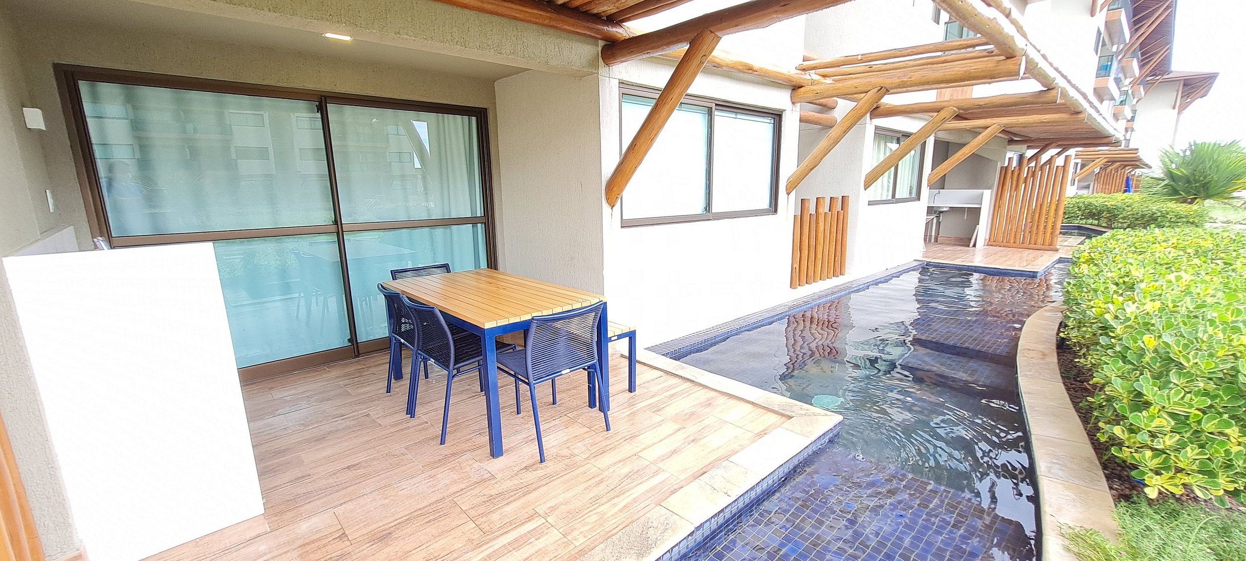 A poolside area with a wooden deck, a table with chairs, and a glass-enclosed room.