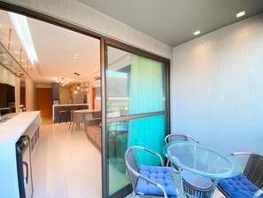 Een moderne keuken met een eethoek, een glazen schuifdeur naar een balkon met rieten stoelen en een glazen tafel.