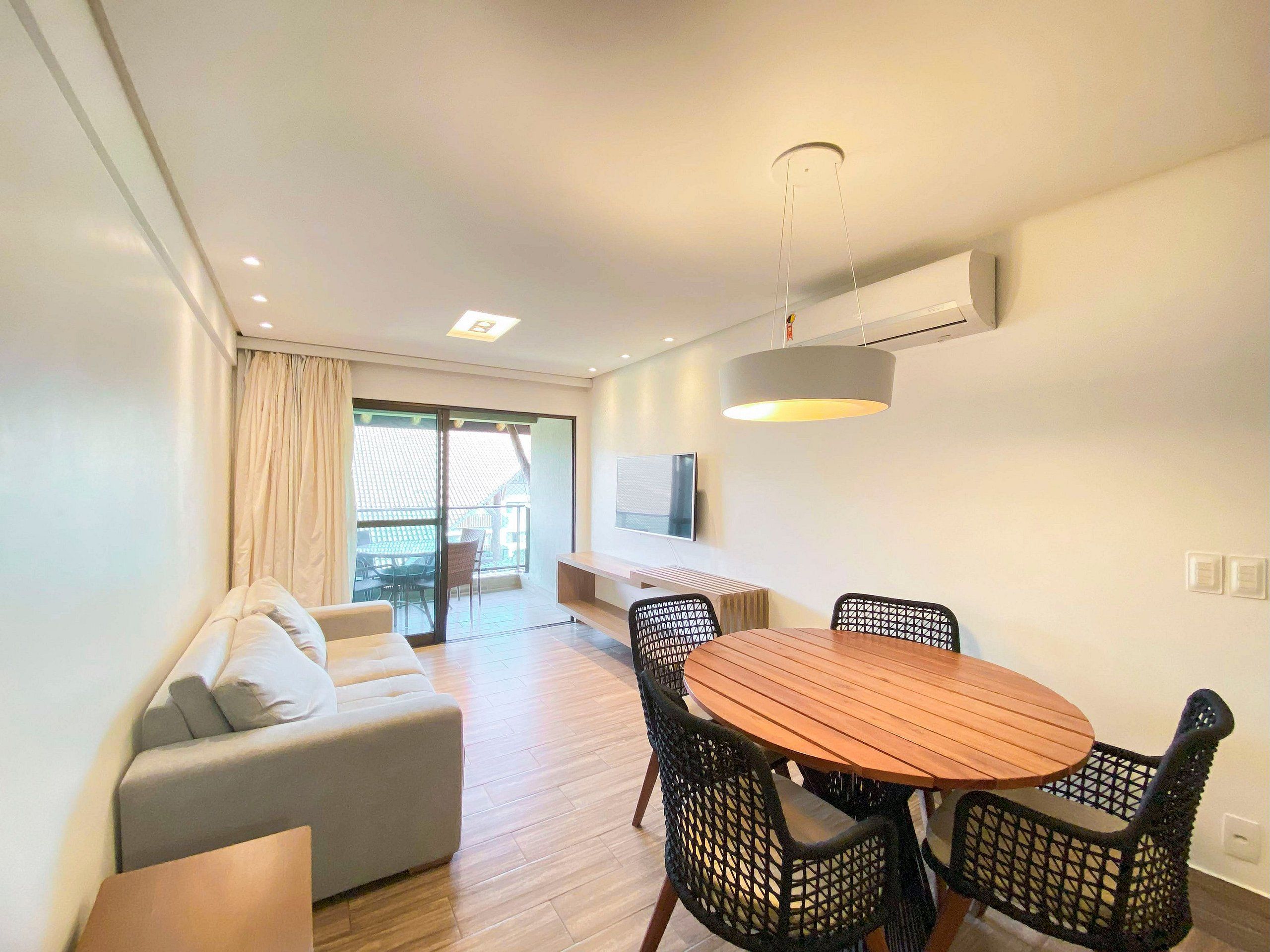 Un salon moderne comprenant un canapé, une table à manger avec des chaises, un luminaire au plafond et un téléviseur fixé au mur.