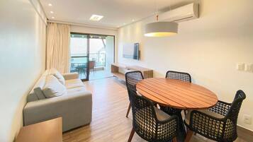 Un salon moderne comprenant un canapé, une table à manger avec des chaises, un luminaire au plafond et un téléviseur fixé au mur.