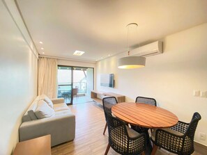 Un salon moderne comprenant un canapé, une table à manger avec des chaises, un luminaire au plafond et un téléviseur fixé au mur.