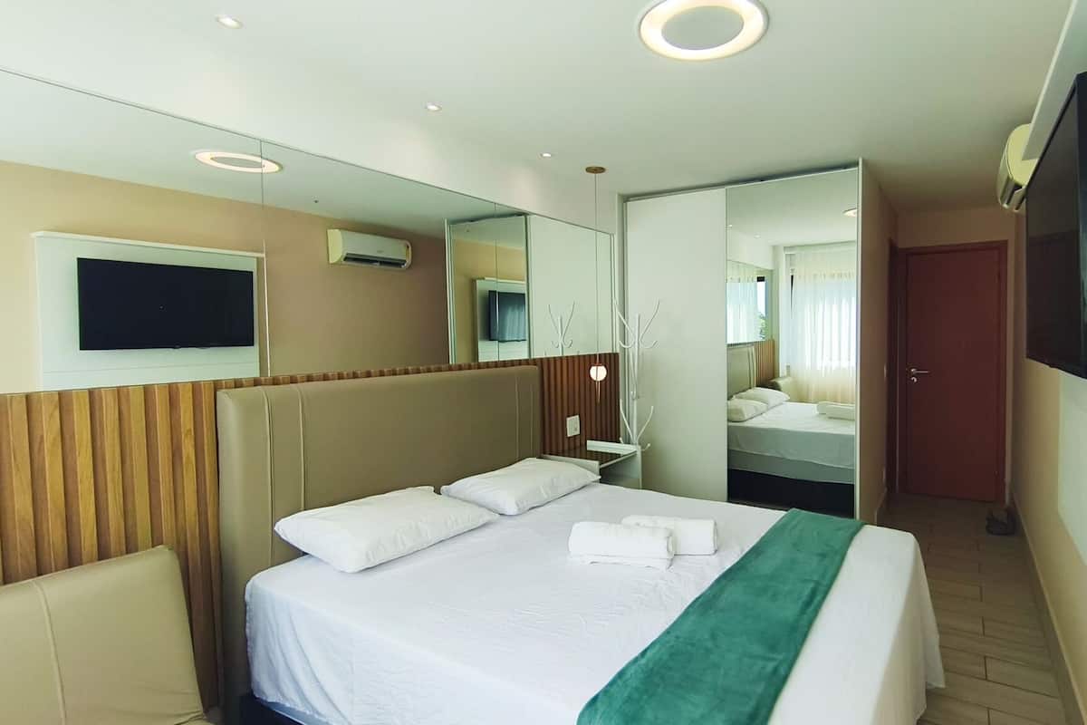 Habitación de hotel con cama, televisión, espejo y puerta que da a un baño.