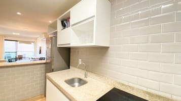 Una cocina moderna con armarios blancos, encimera de granito, pileta de acero inoxidable y placa de inducción negra.