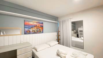 Une chambre d’hôtel avec un lit, une commode, un tableau, un miroir et une fenêtre avec des rideaux.