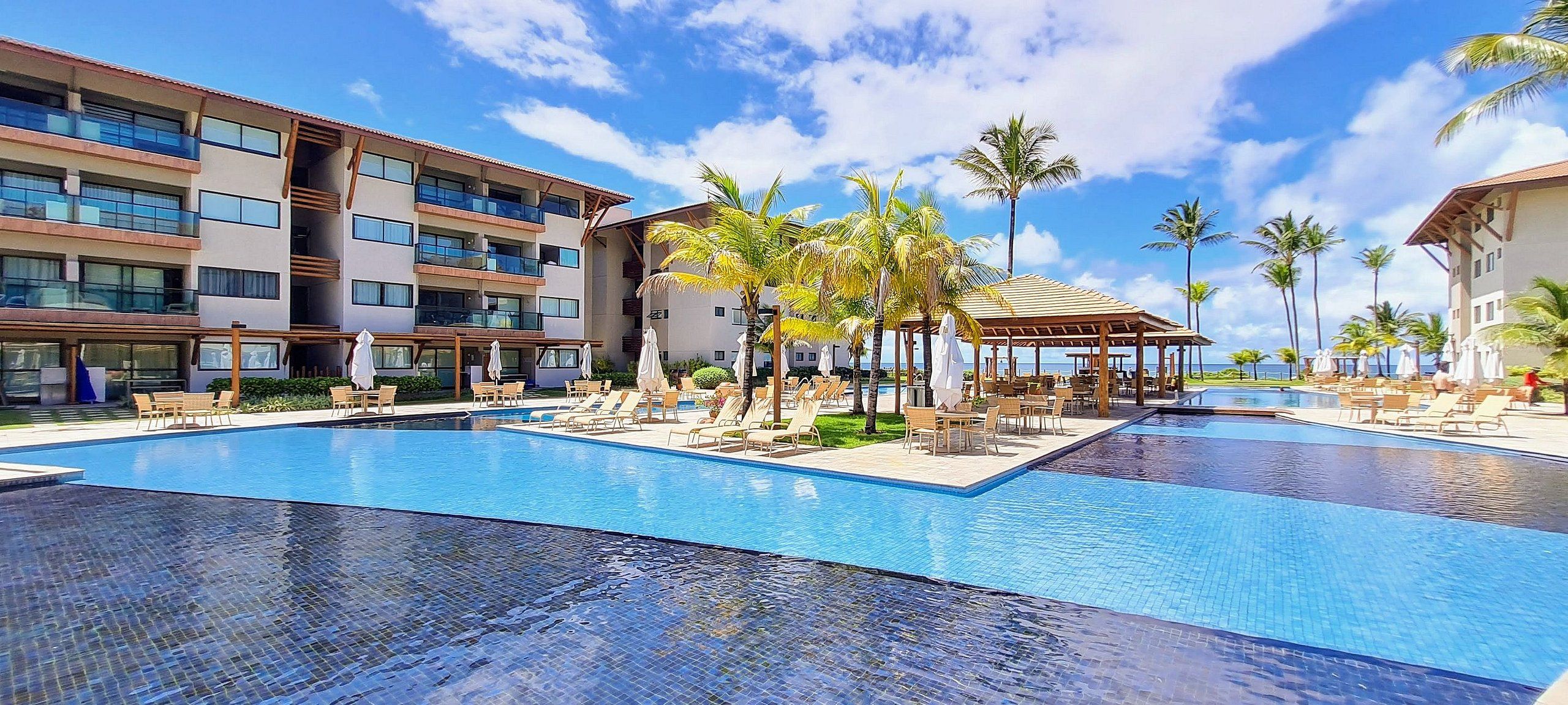 Et hotel med flere swimmingpools, udendørs siddepladser og palmer.