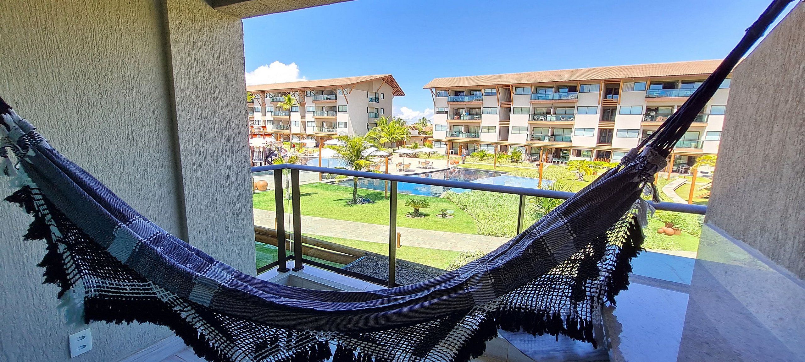 Un'amaca su un balcone con vista su una piscina e un complesso di edifici.