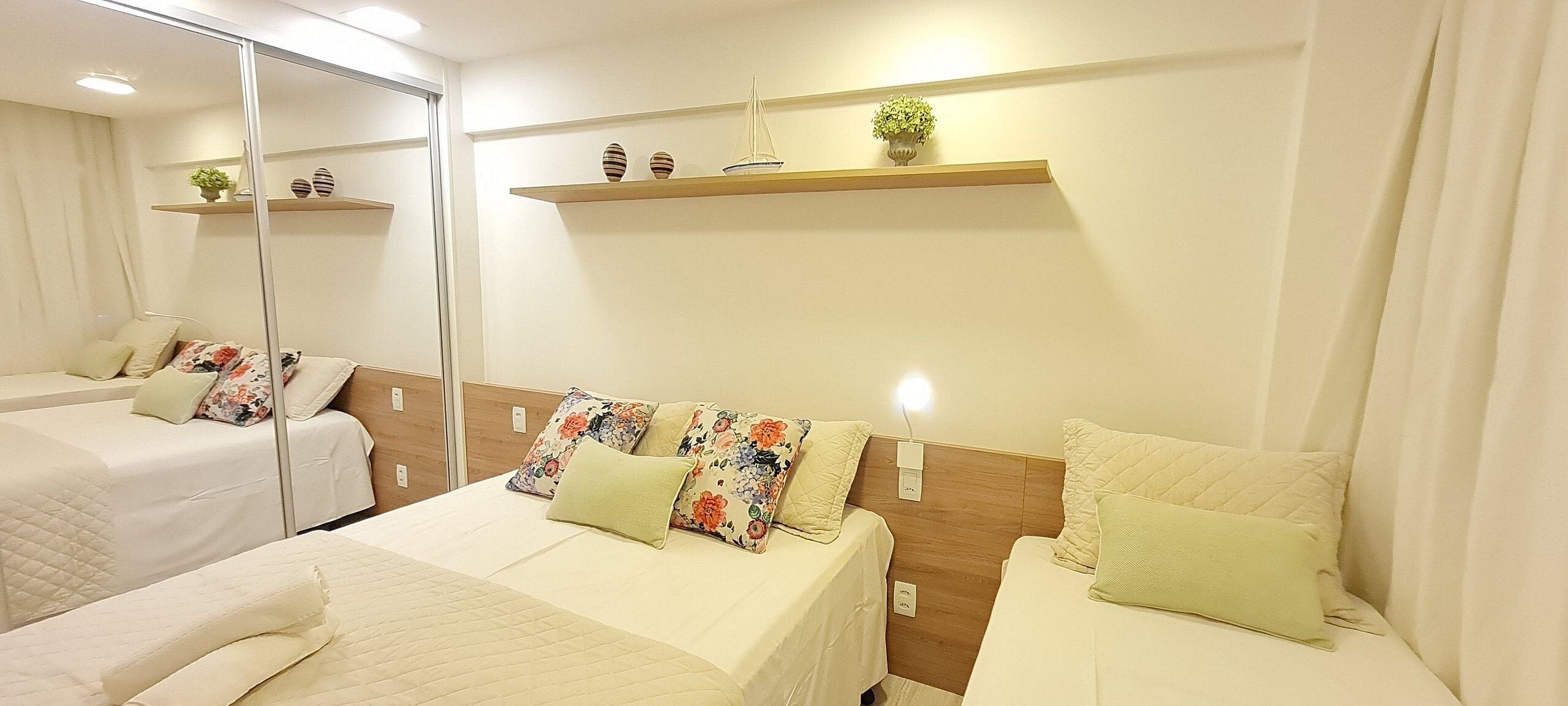 Une chambre d’hôtel avec deux lits, un miroir, une tête de lit en bois et une étagère ornée d’objets décoratifs.
