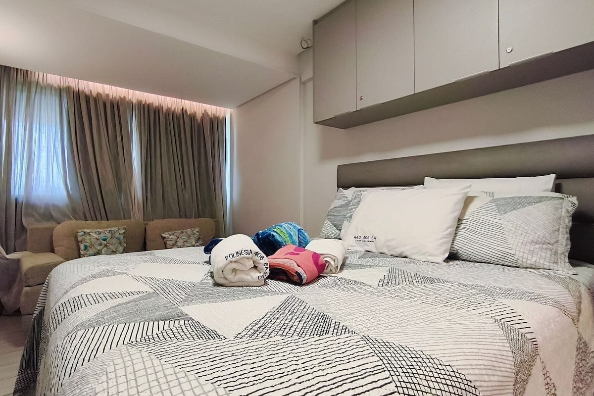 Una habitación de hotel con cama, sofá, ventana con cortinas y cabecero.