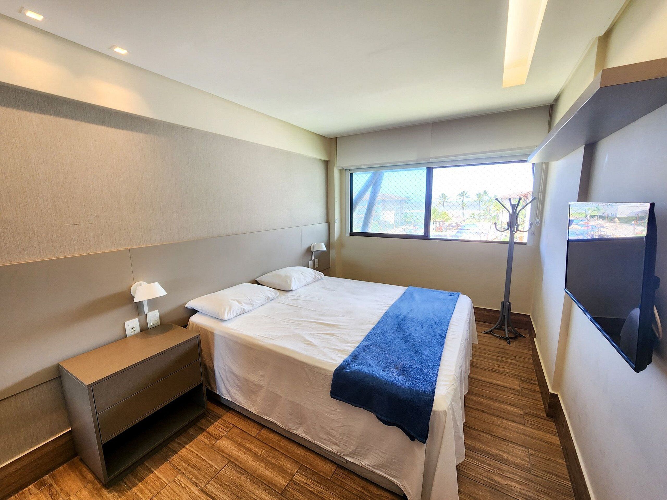 Une chambre d’hôtel moderne équipée d’un lit, d’une table de chevet, d’une lampe et d’un téléviseur fixé au mur.