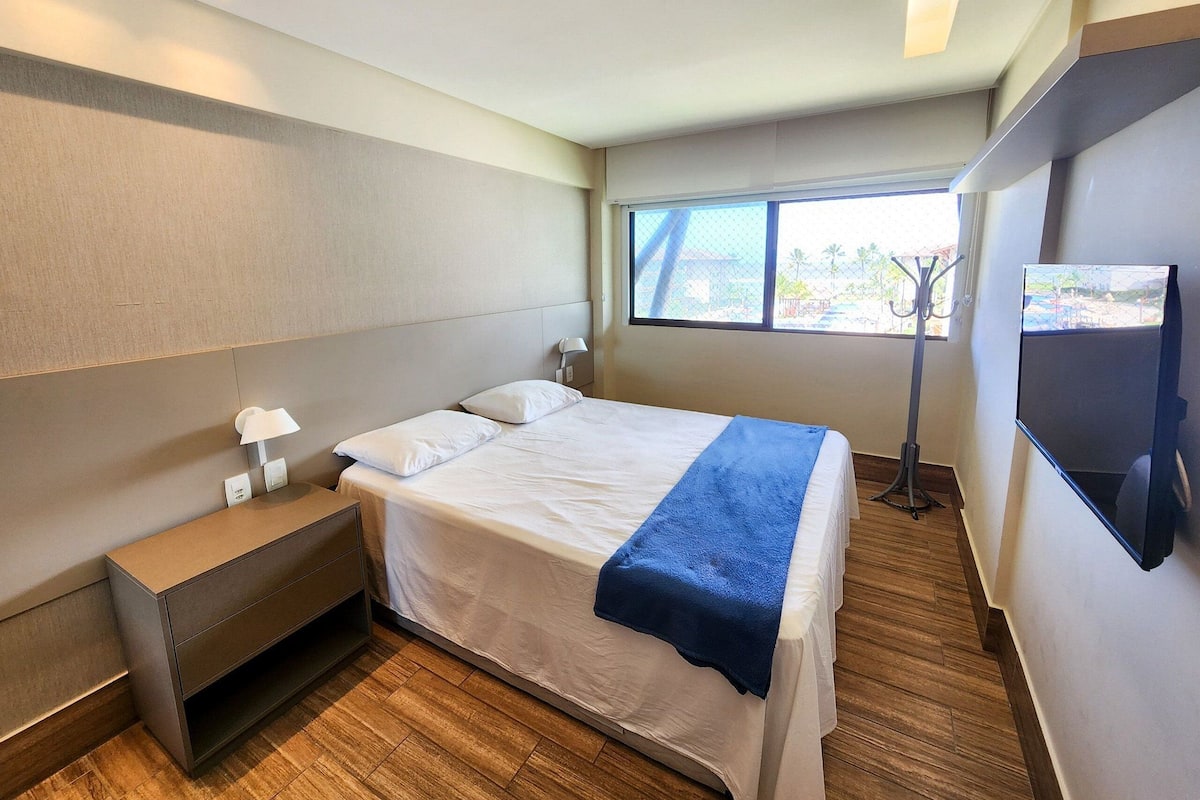 Una habitación de hotel moderna con una cama, mesita de noche, lámpara y un televisor montado en la pared.