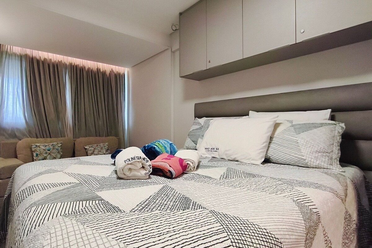 A hotel room with a bed, a sofa, a window with curtains, and a headboard.