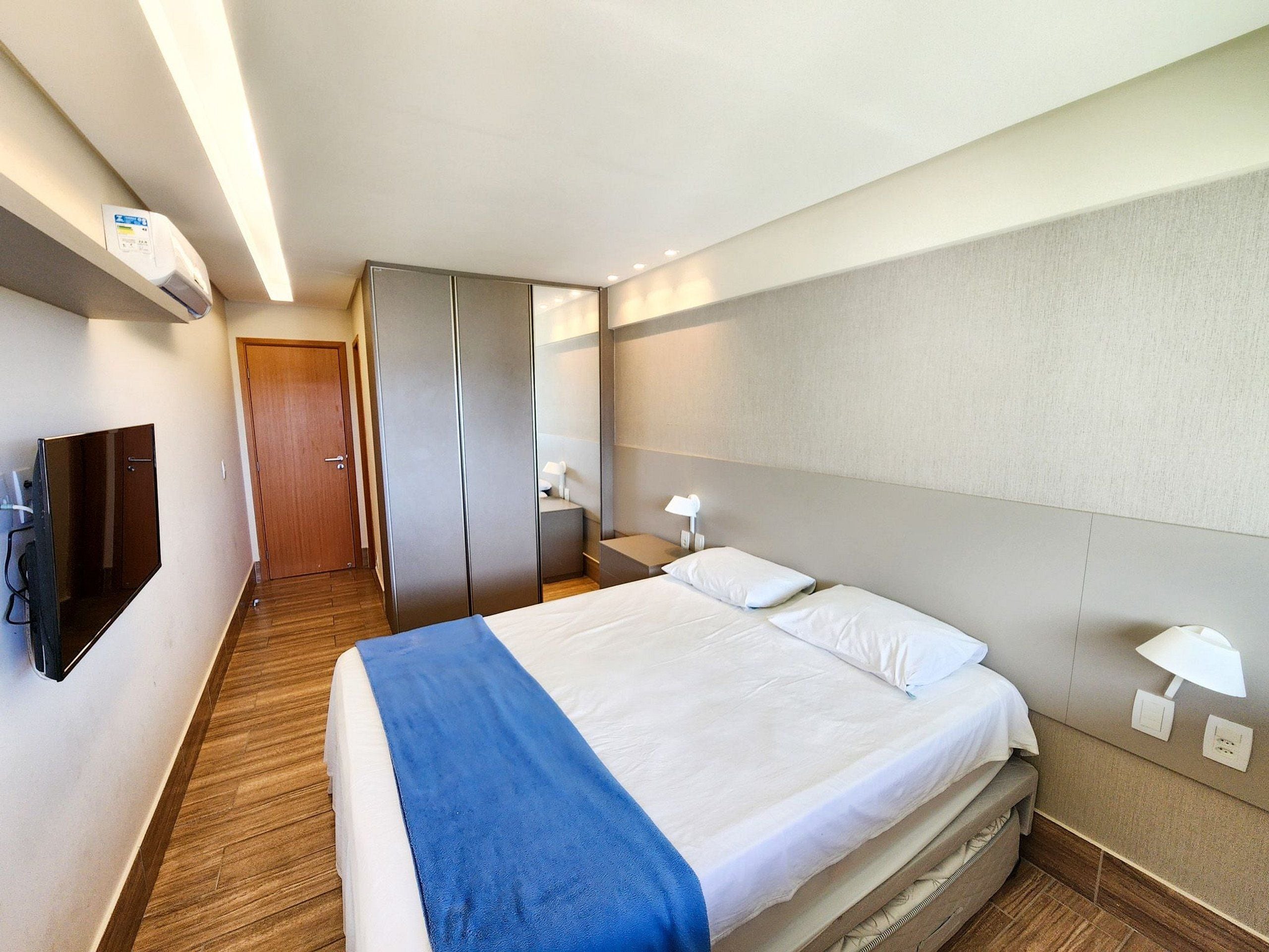 A hotel room with a bed, a TV, a wardrobe, and a desk with a lamp.
