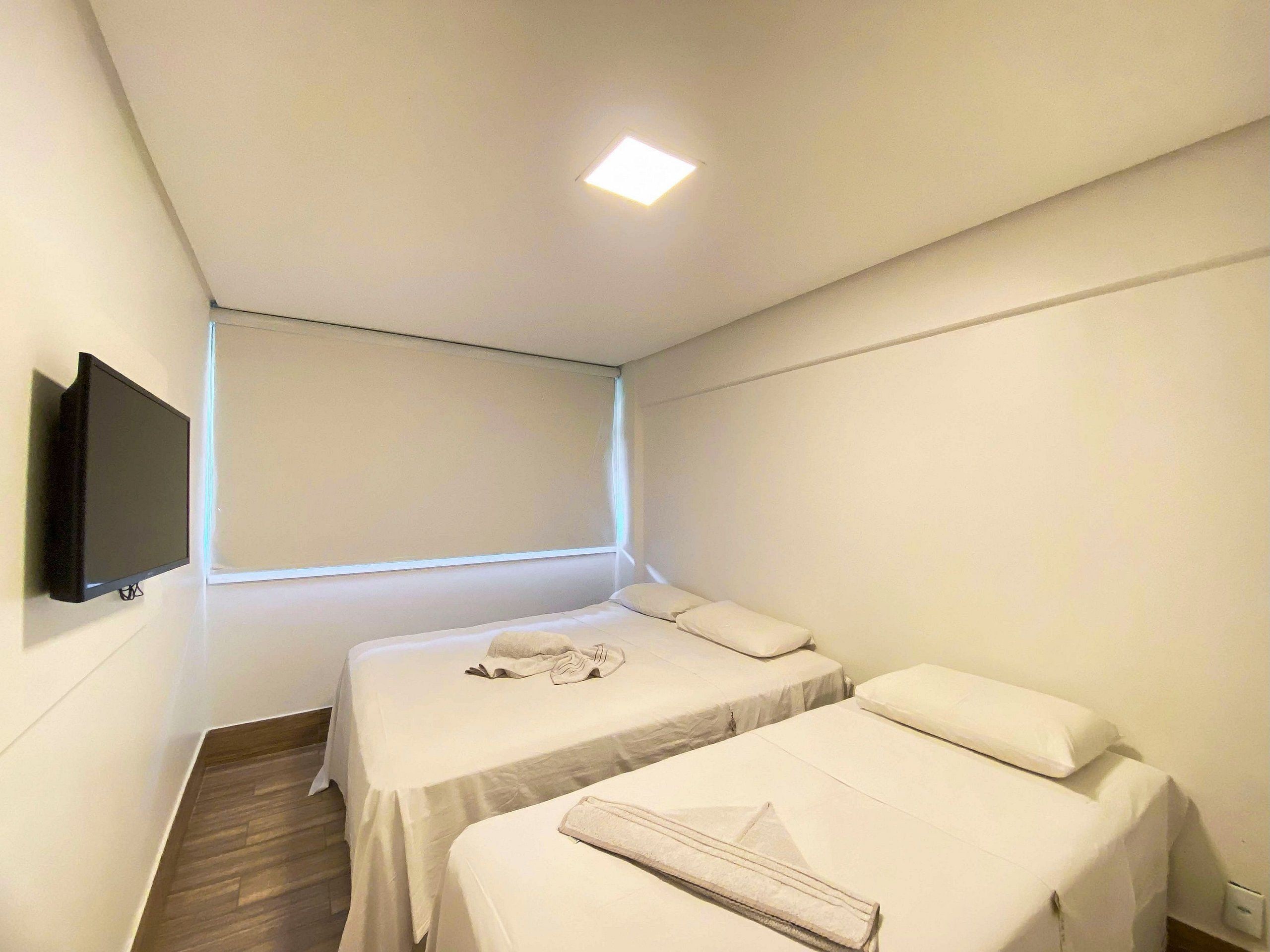 Ein Hotelzimmer mit zwei Betten, einem an der Wand befestigten Flachbildfernseher und einem Fenster, das für natürliches Licht sorgt.