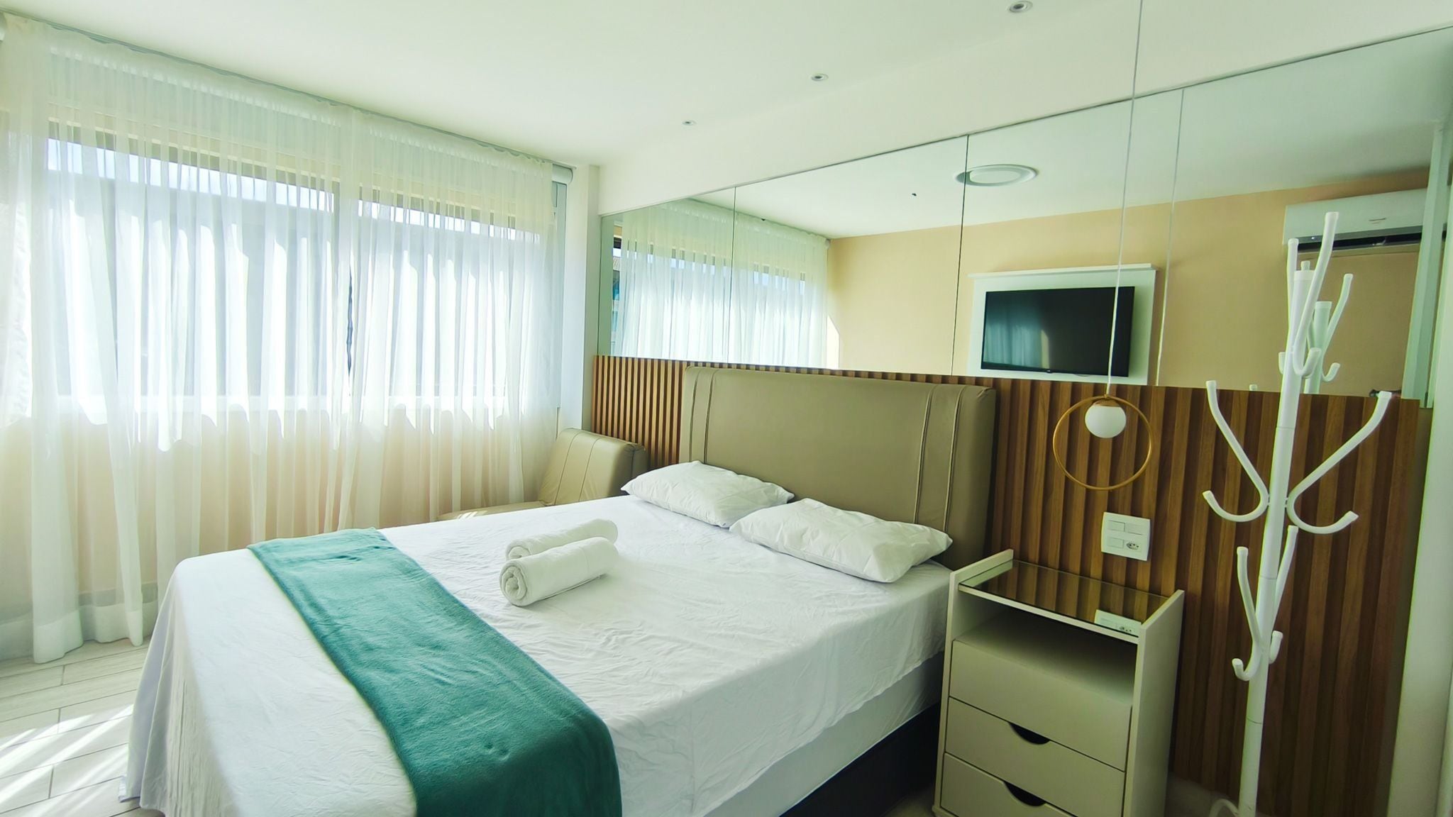 A hotel room with a bed, a TV, a mirror, and a coat rack.