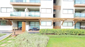 Un edificio de varios pisos con balcones, una zona de estar al aire libre techada y un jardín cuidado.