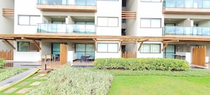 A multi-story building with balconies, a covered outdoor seating area, and a well-maintained garden. - Flats no La Fleur Polinésia Residence (Ipojuca)