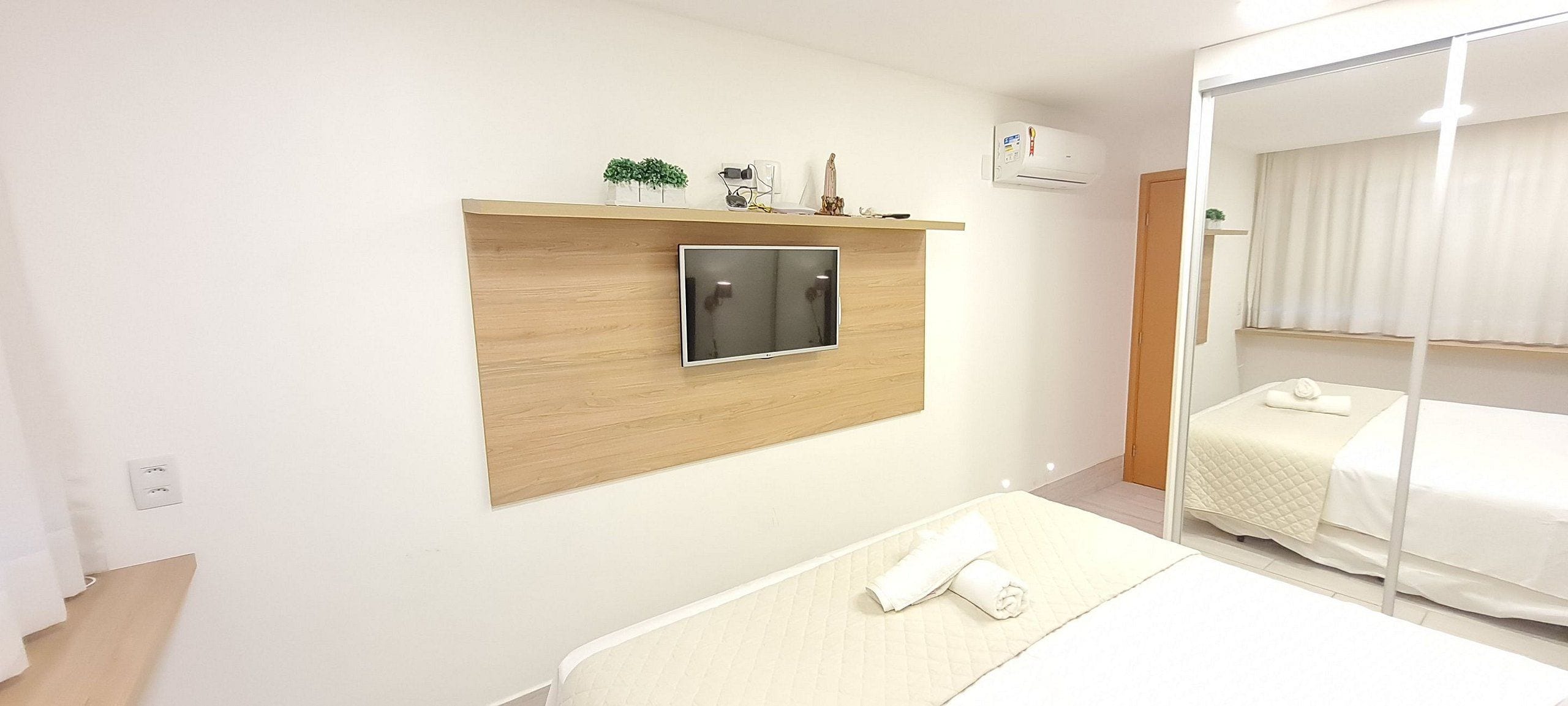 Una habitación de hotel con una cama, un televisor montado en un panel de madera, un espejo y un armario.