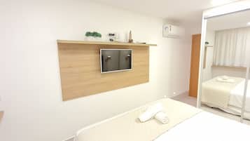 Una habitación de hotel con una cama, un televisor montado en un panel de madera, un espejo y un armario.