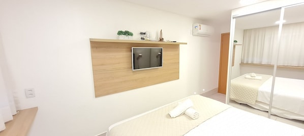 A hotel room with a bed, a TV mounted on a wooden panel, a mirror, and a wardrobe.