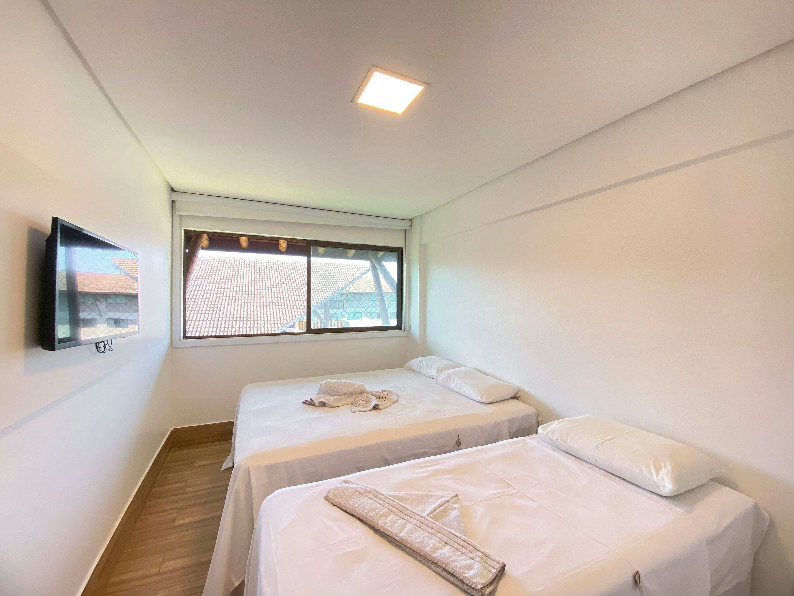 Une chambre avec deux lits, un téléviseur fixé au mur et une fenêtre donnant sur des immeubles.