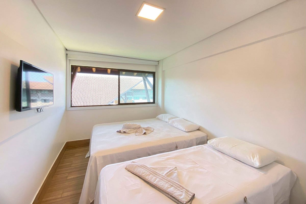 Una habitación con dos camas, un televisor montado en la pared y una ventana con vistas a edificios.