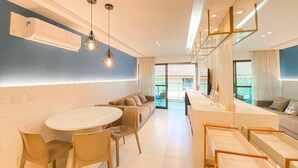 A modern hotel room with a dining area, a sofa set, and a view of the outside. - Flats no La Fleur Polinésia Residence (Ipojuca)