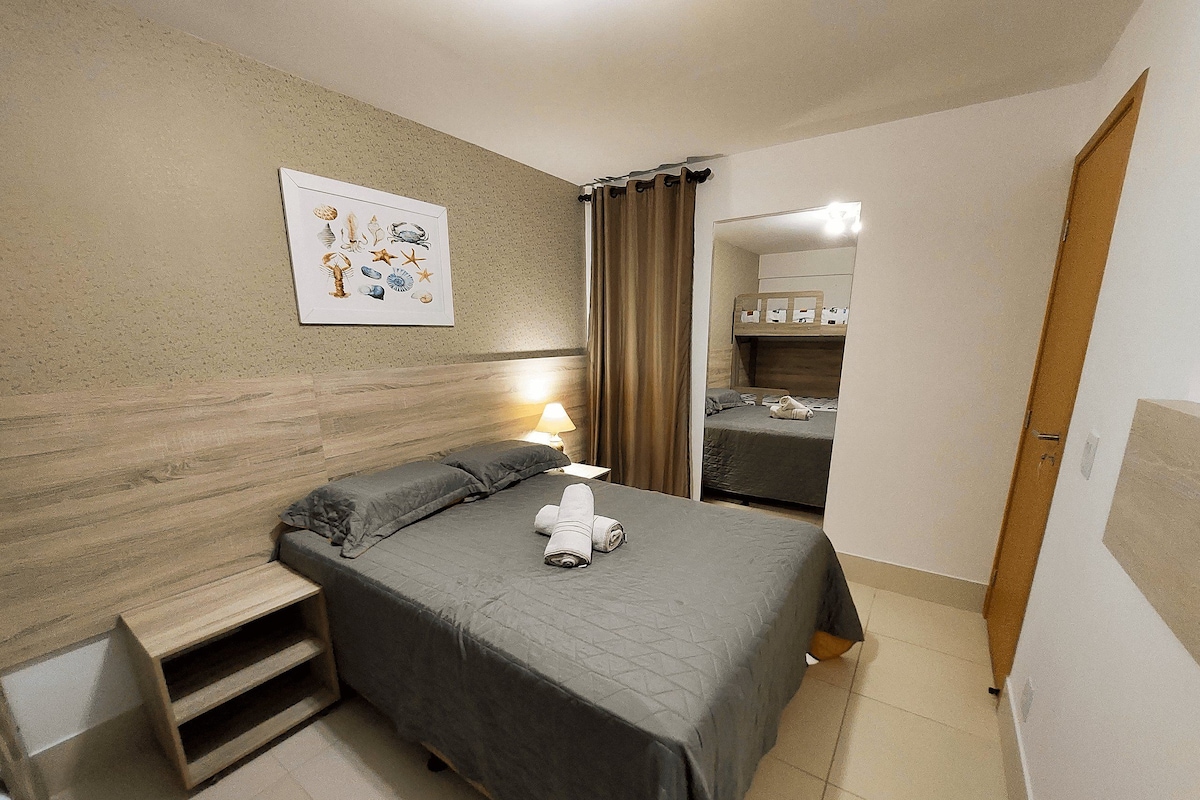 A bedroom with a bed, a nightstand, a lamp, a wall-mounted picture, and a wooden door.
