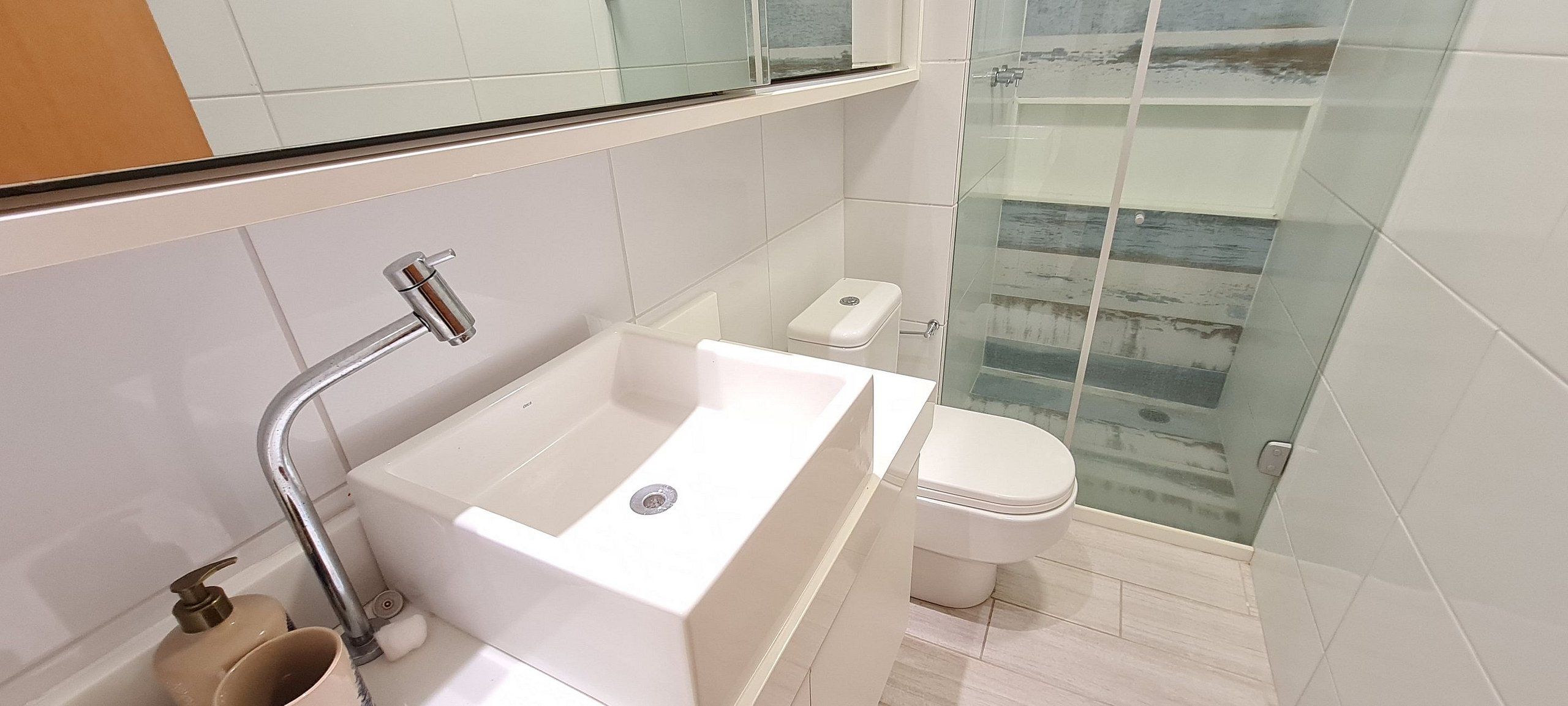 A modern bathroom with a white sink, toilet, and glass shower enclosure.