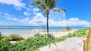 A beach with a wooden fence, palm trees, and a clear sky. - Flats no La Fleur Polinésia Residence (Ipojuca)