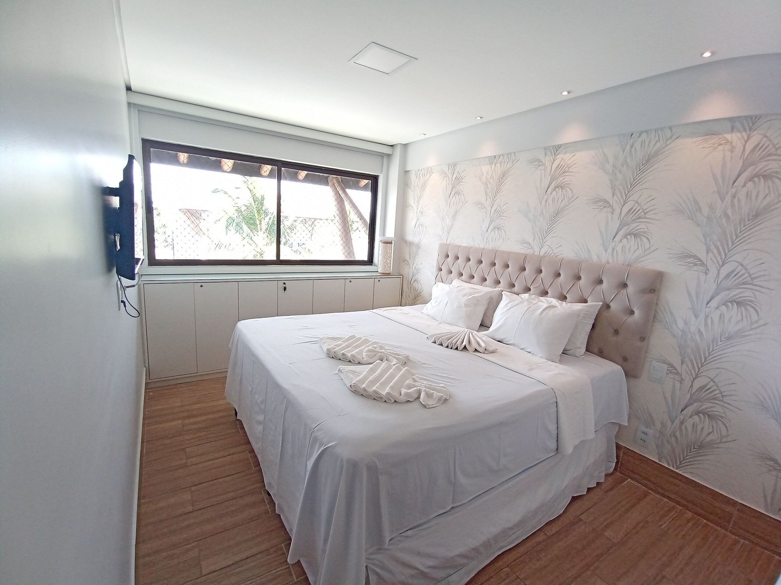Une chambre avec un grand lit, une fenêtre et un mur orné d’un motif de feuilles.