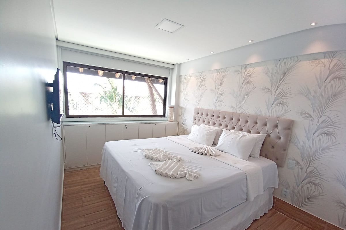 Un dormitorio con una cama grande, una ventana y una pared con diseño de hojas.