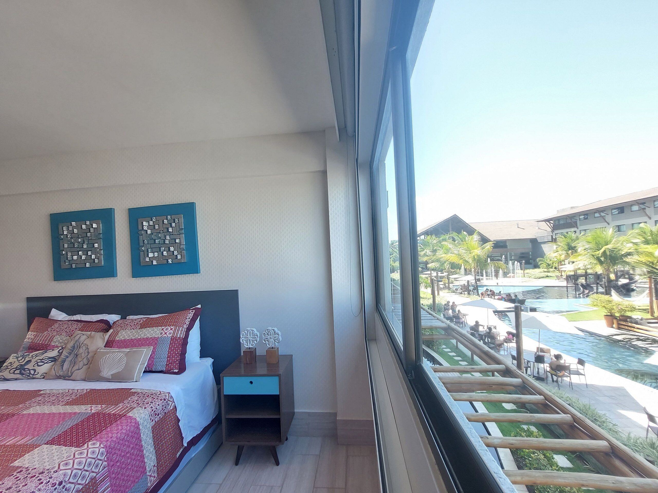 Une chambre avec un lit, une table de chevet et des œuvres d’art murales, donnant sur un espace piscine aménagé avec des sièges d’extérieur.