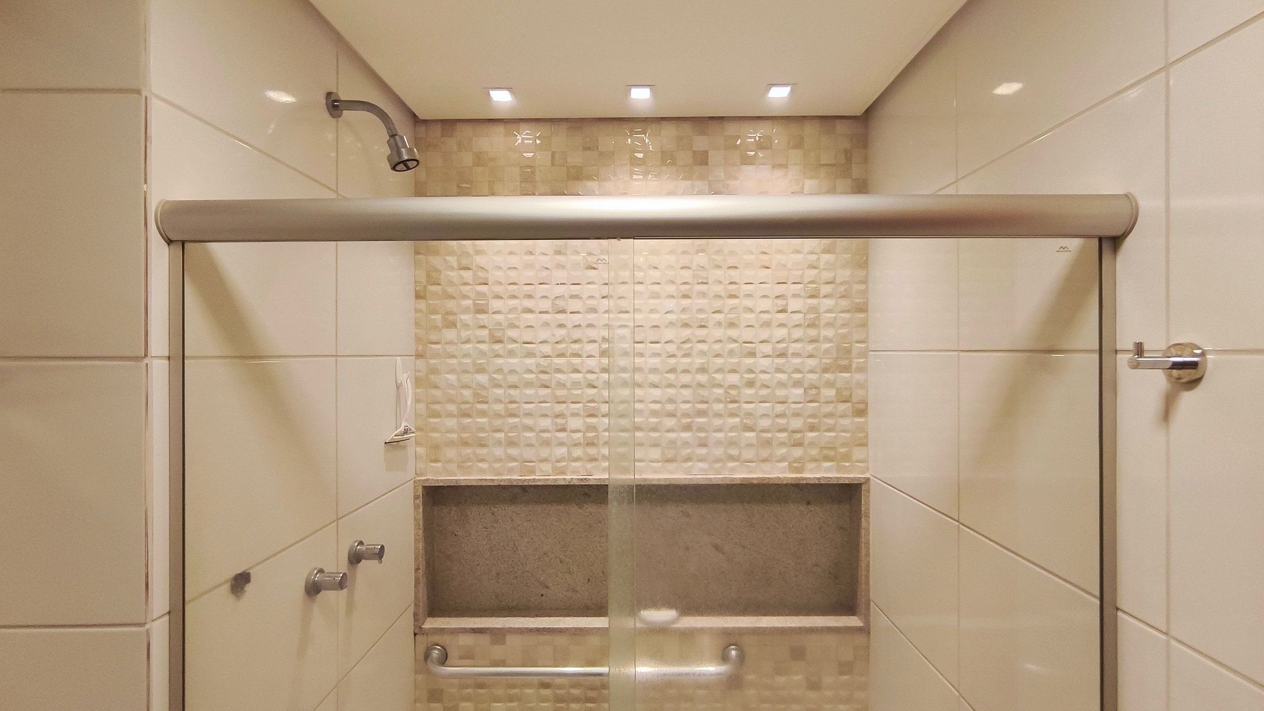 A walk-in shower with a glass door, a tiled wall with a textured pattern, and a ceiling with recessed lighting.