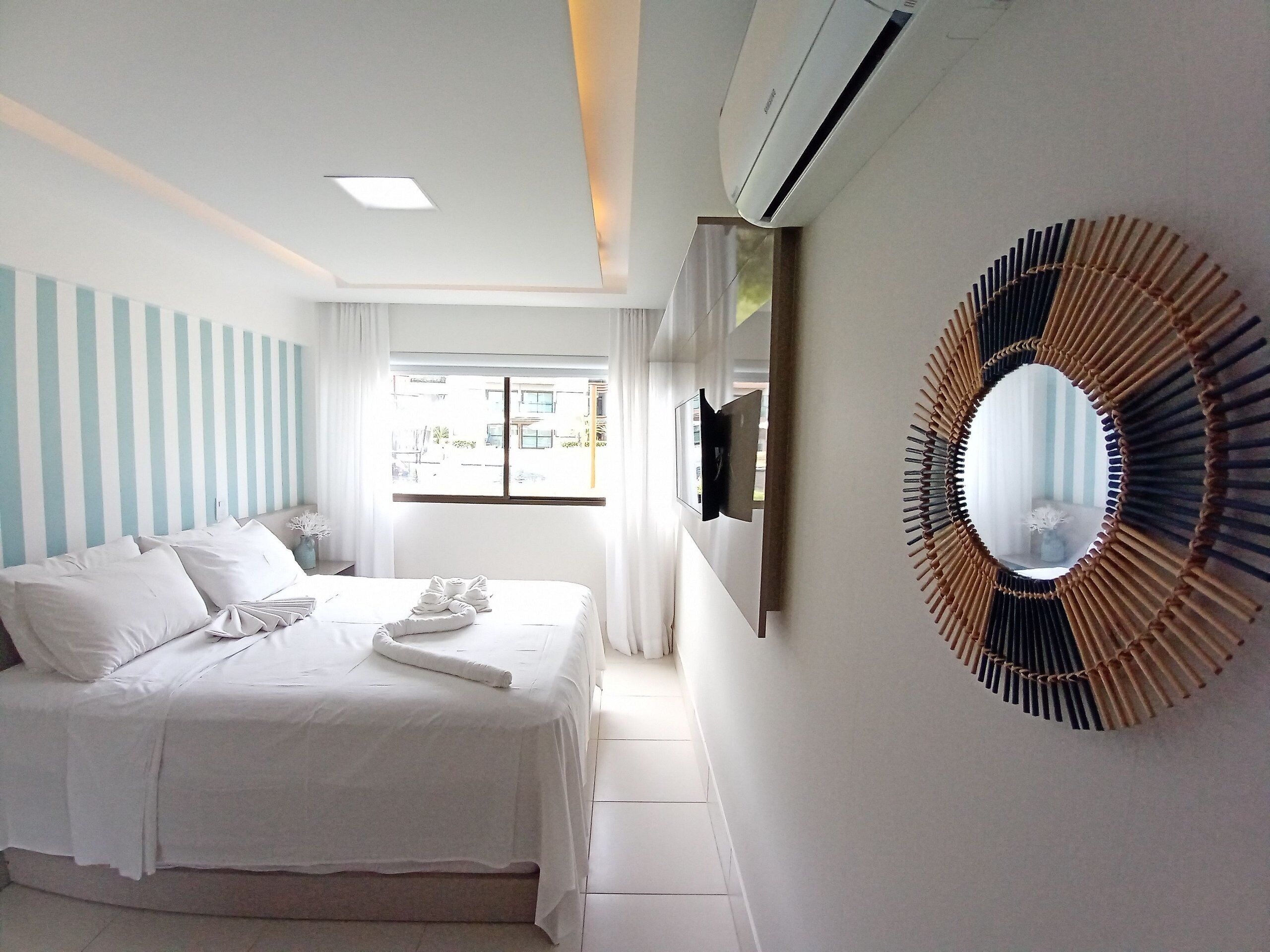 Une chambre d’hôtel avec un lit, un téléviseur fixé au mur, un grand miroir et une fenêtre avec des rideaux.