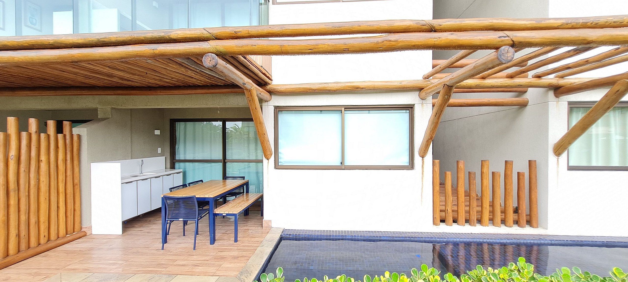 A modern outdoor patio with a wooden pergola, a pool, and a dining area with a table and chairs.
