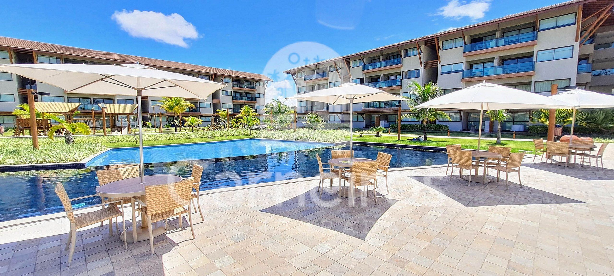 A hotel with a swimming pool, outdoor seating, and a multi-story building with balconies.