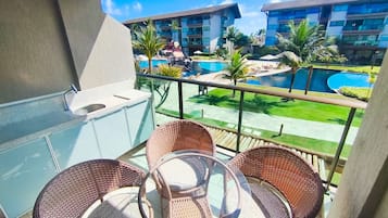 Un balcón con sillas de mimbre, una piscina y vistas a edificios de hotel.
