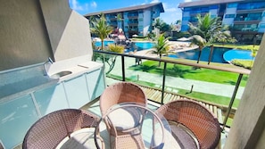 A balcony with wicker chairs, a pool, and a view of hotel buildings.