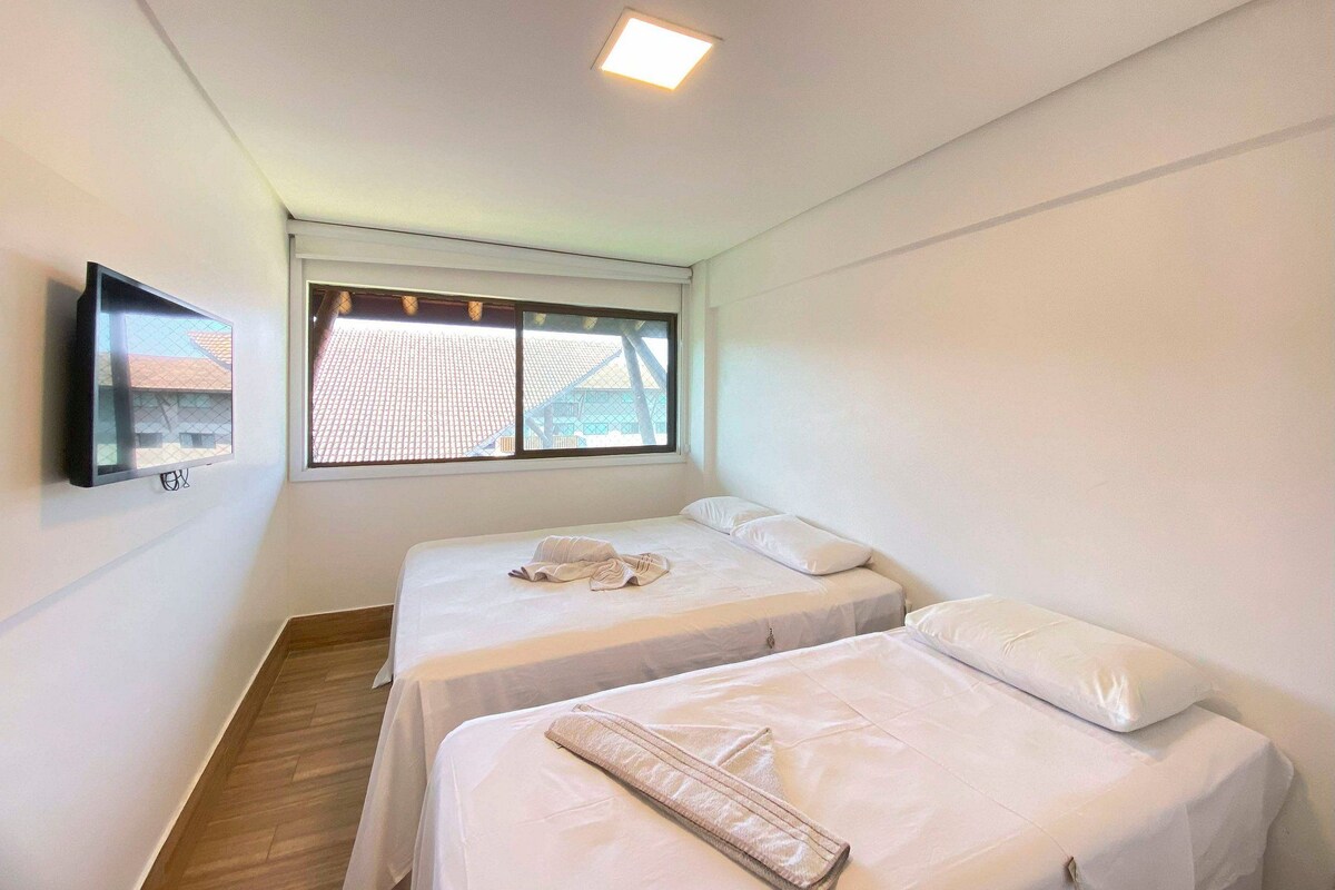 A room with two beds, a TV mounted on the wall, and a window with a view of buildings.