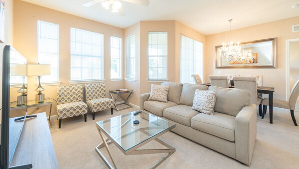 A living room with a beige sofa, patterned armchairs, a glass coffee table, and a chandelier. - Stunning, Newly Renovated Condo, Near Disney and Universal (Davenport)