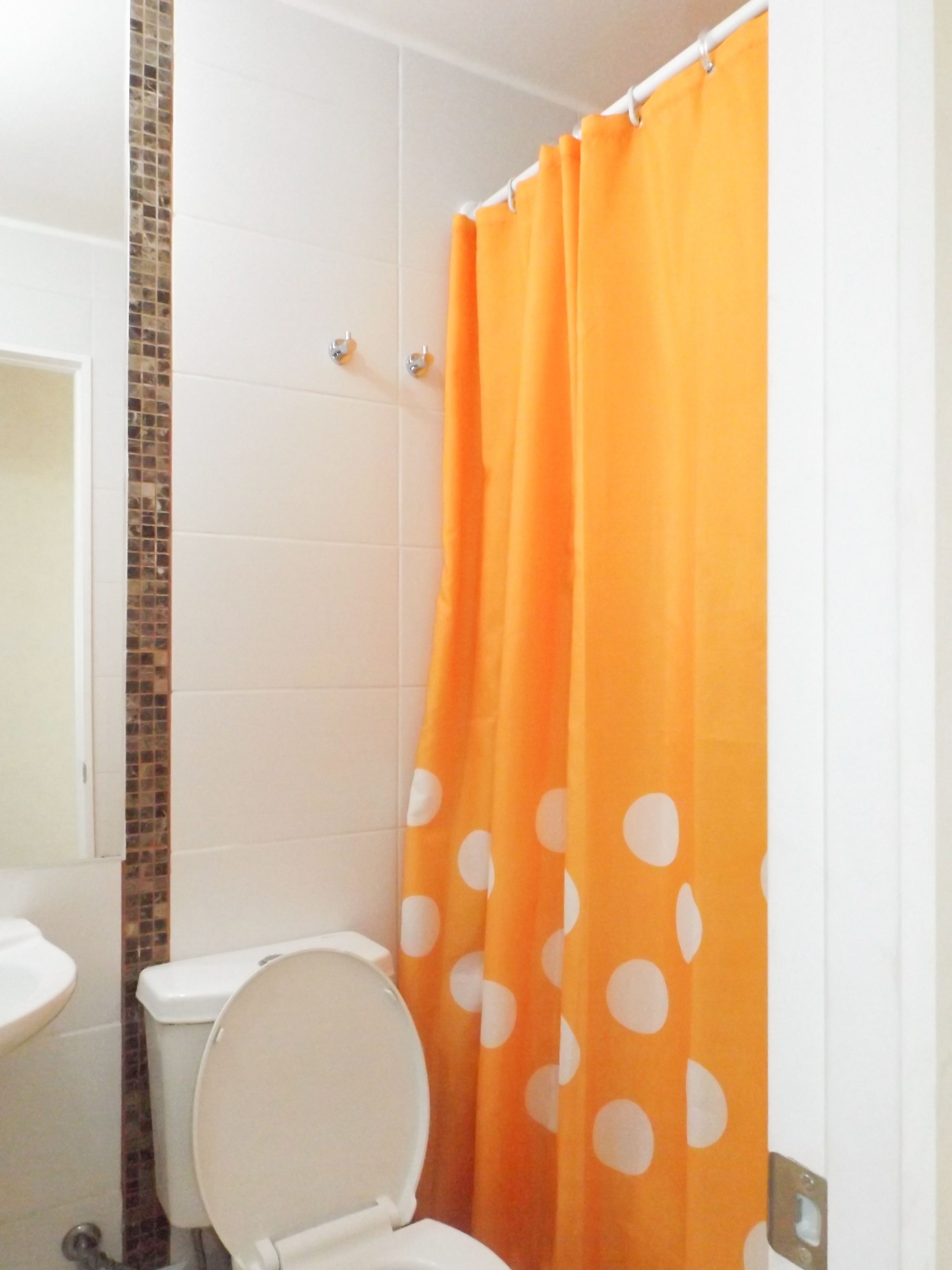 A bathroom with a white toilet, a shower curtain with orange polka dots, and a tiled wall.