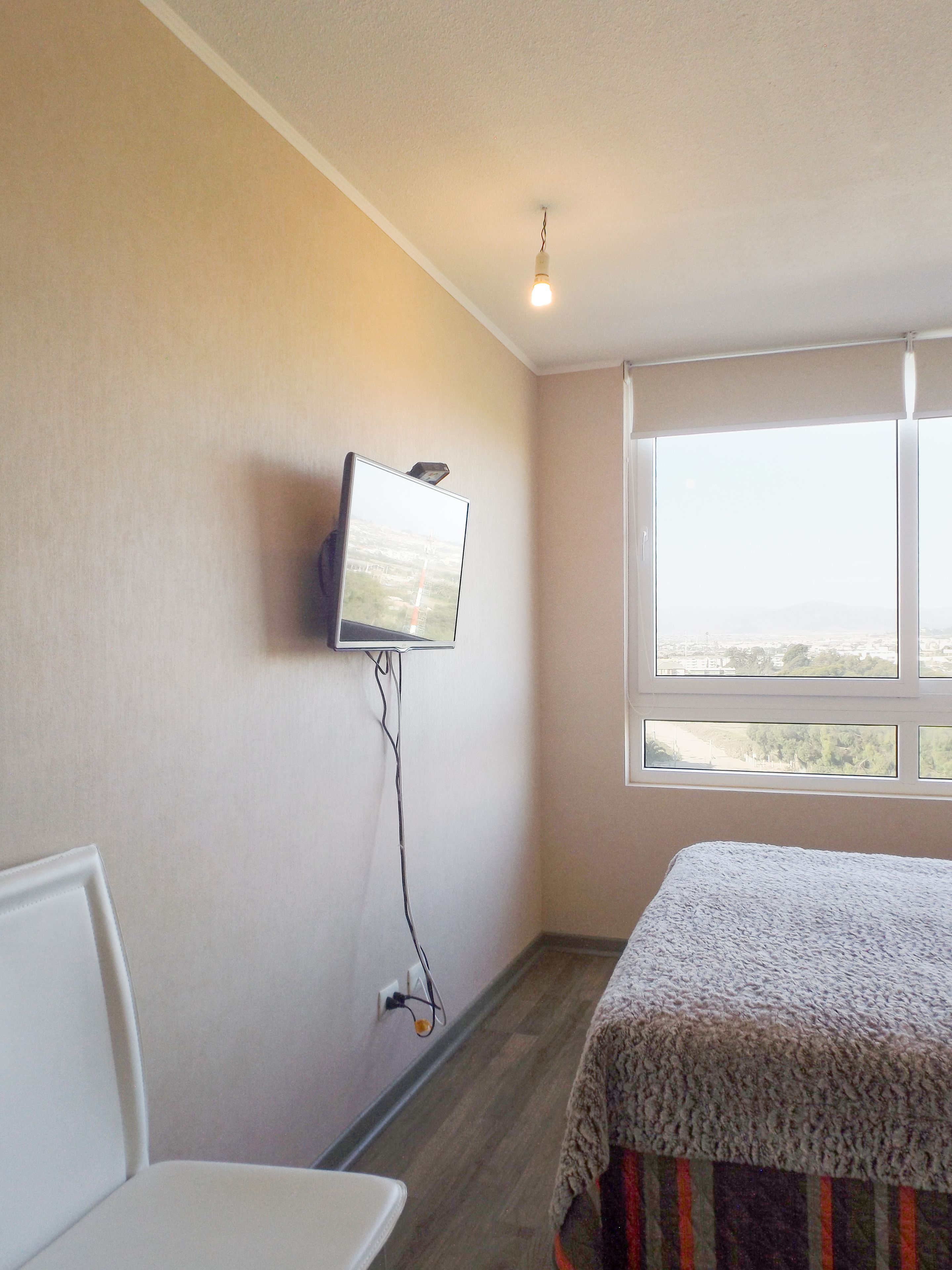 Une chambre d’hôtel avec un lit, un téléviseur fixé au mur, une fenêtre donnant sur un paysage agréable et un fauteuil.