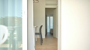 A hallway with wooden flooring, a chair, and a table. - West Village Appartamento - NUOVO con piscina (Jesolo)
